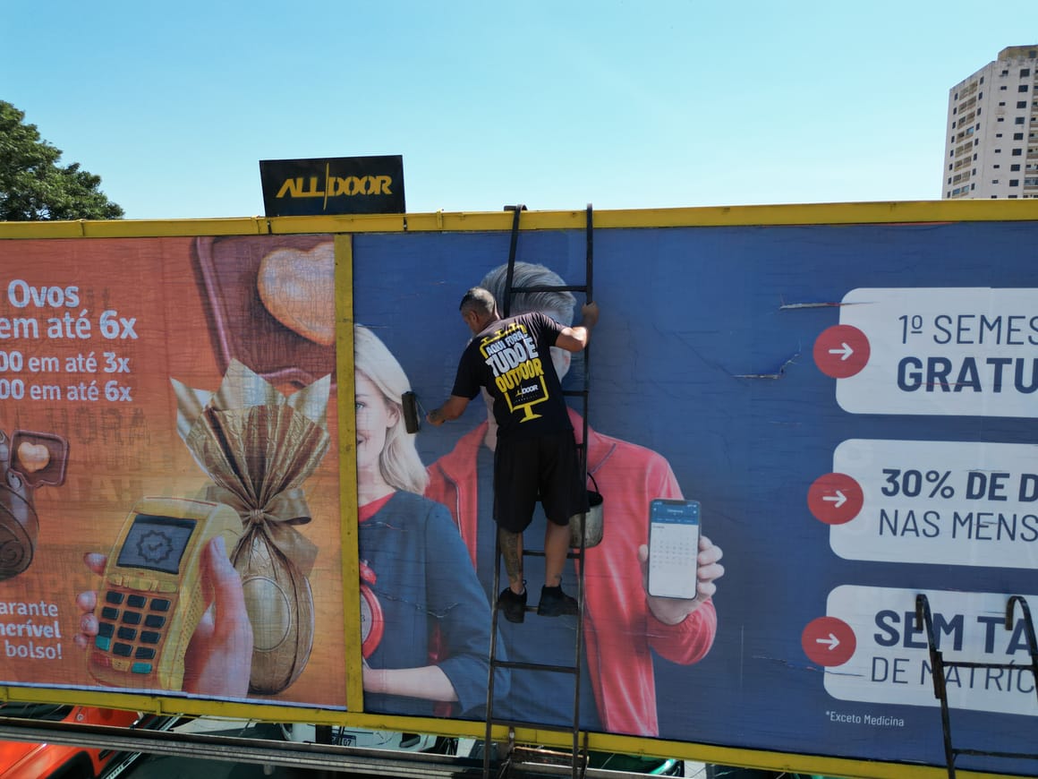 Colador da AllDoor aplicando o papel em um outdoor